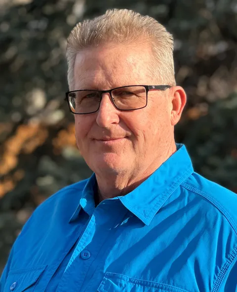 Stephen Abbot smiling in a red plaid shirt and tortoise shell glasses